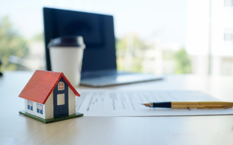 Image of a small property with a laptop, pen and paper and a paper cup
