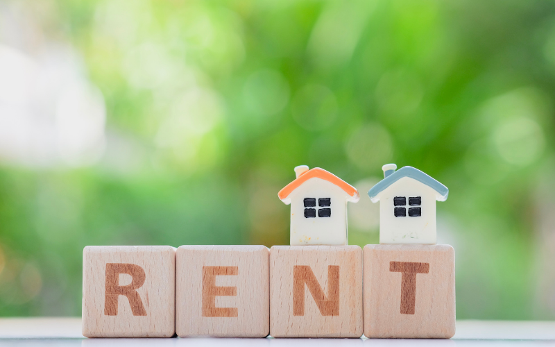 2 small houses on top of word blocks with the word "rent" and a green background